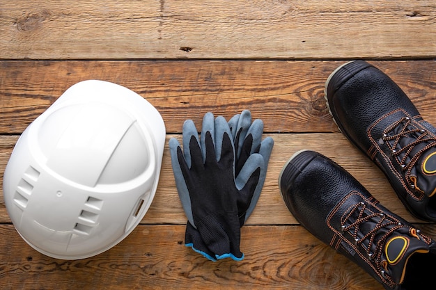 Botas y guantes de casco de trabajo en una vista superior de fondo de madera