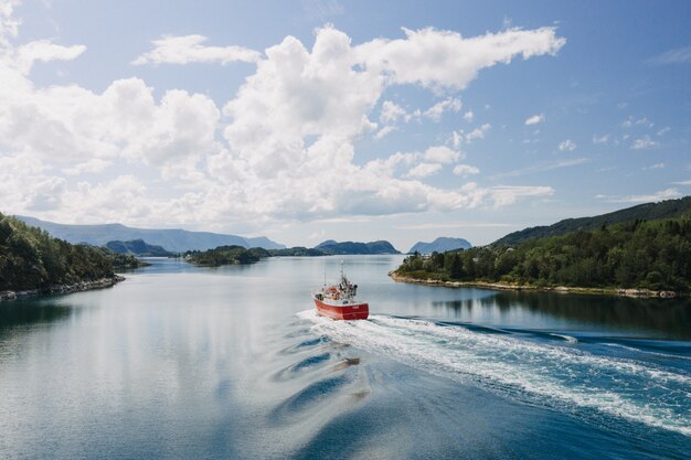 Un bote en el cuerpo del agua rodeado de árboles bajo un cielo azul claro con nubes blancas