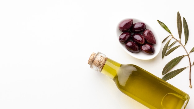 Botella de aceite de oliva con hojas y aceitunas moradas con espacio de copia