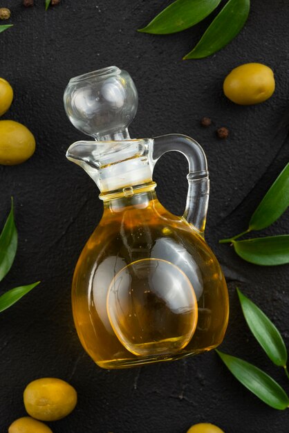 Botella de aceite de oliva en la mesa con hojas y aceitunas