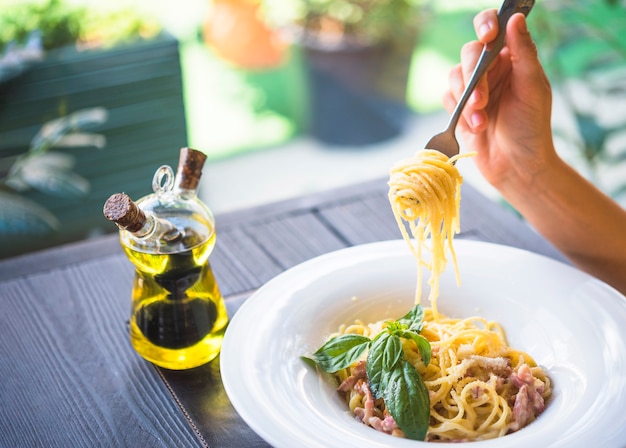 Botella de aceite de oliva con una persona con espaguetis con un tenedor.