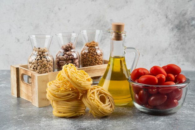 Una botella de aceite con pasta nido cruda y tomates cherry.