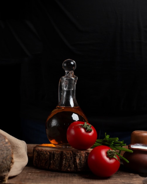 Botella de aceite, tomates y hierbas en la pieza de madera.