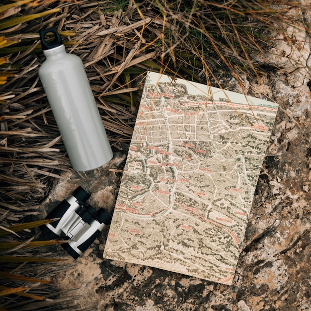 Botella de agua; binoculares y mapa en roca cerca de la hierba