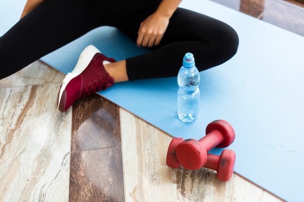 Botella de agua y pesas en colchoneta de yoga