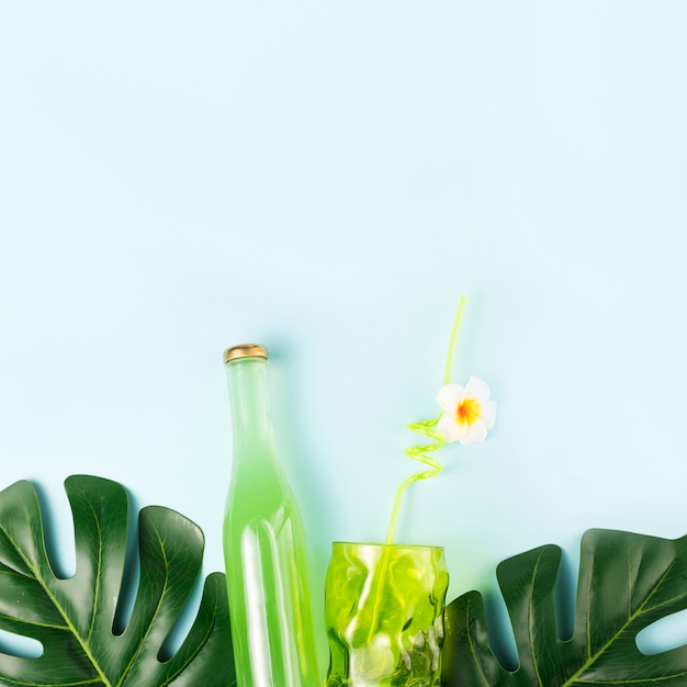 Foto gratuita botella de bebida cerca de vaso con paja y plantas verdes.