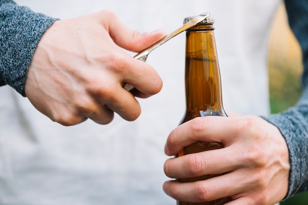 Botella de cerveza de apertura de mano de una persona con el abrelatas