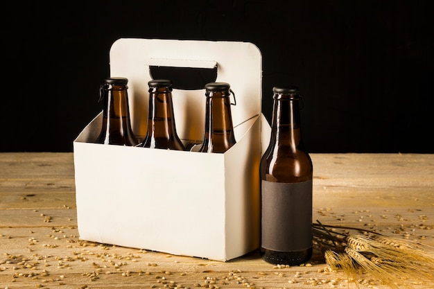 Botella de cerveza caja de cartón y espigas de trigo en superficie de madera