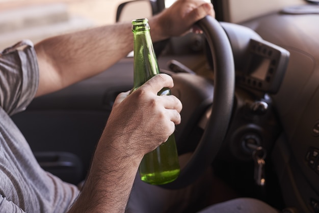 Botella de cerveza en manos de un hombre conduciendo el coche durante el día