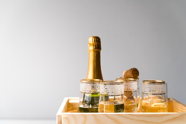 Botella de Champagne y copas en cajón de madera sobre fondo blanco.