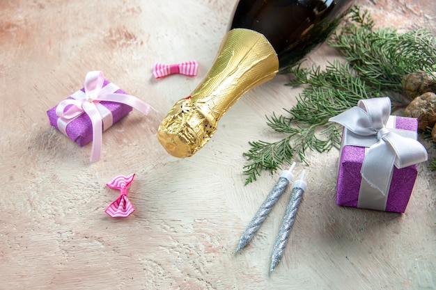 Botella de champán vista frontal con pequeños regalos sobre fondo claro