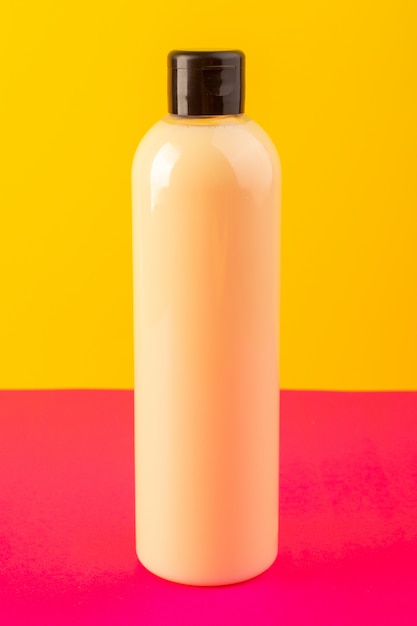 Una botella de champú de plástico de color crema con vista frontal puede con tapa negra aislada en el fondo rosa-amarillo cosméticos belleza cabello