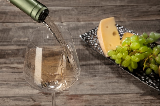 Una botella y una copa de vino blanco con frutas sobre mesa de madera
