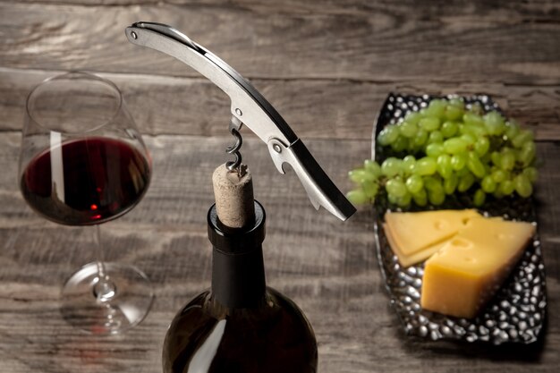 Una botella y una copa de vino tinto con frutas sobre mesa de madera