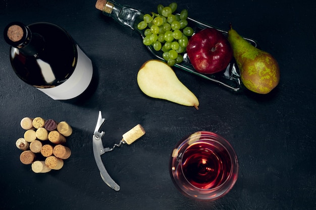 Una botella y una copa de vino tinto con frutas sobre la superficie de piedra oscura