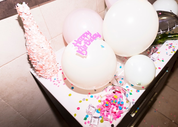 Botella cubierta de confeti rosa contra globo blanco.