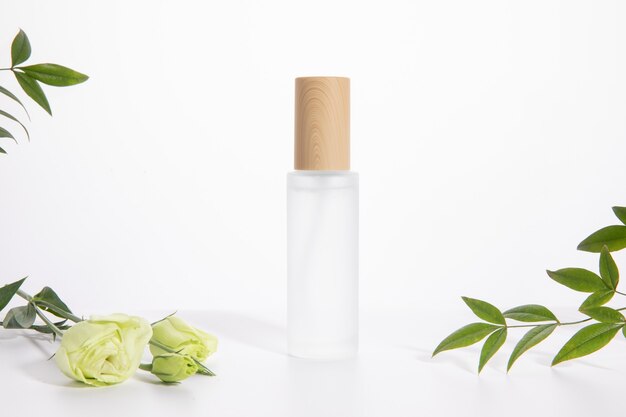 Botella de cuidado de la piel individual sobre un fondo blanco con una rosa y hojas verdes