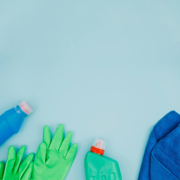 Botella de detergente; Guantes verdes y servilleta azul sobre fondo azul