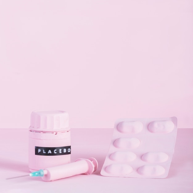Botella de jeringa, ampolla de píldora y placebo sobre fondo rosa