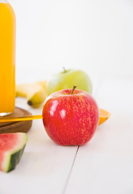 Botella de jugo y manzana roja entera fresca en escritorio de madera blanco