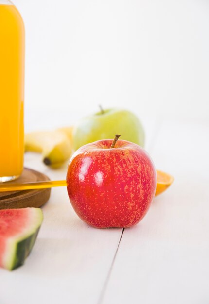 Botella de jugo y manzana roja entera fresca en escritorio de madera blanco