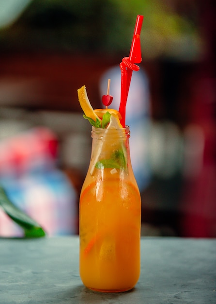 Foto gratuita una botella de jugo de naranja con rodajas de naranja y paja de plástico rojo