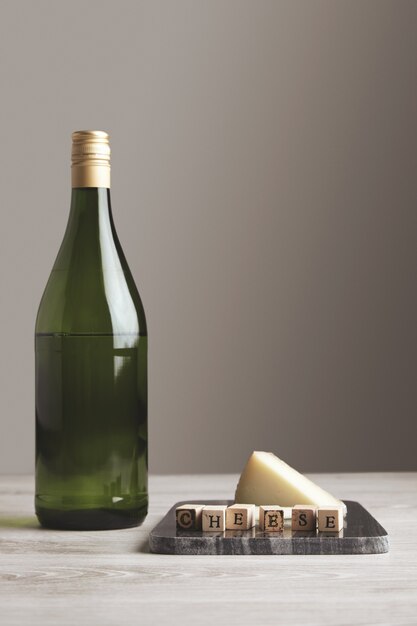 Botella de jugo de vino de uva verde cerca de tablero de mármol de piedra con letras de madera queso y queso de cabra en él aislado en blanco fondo en blanco y mesa