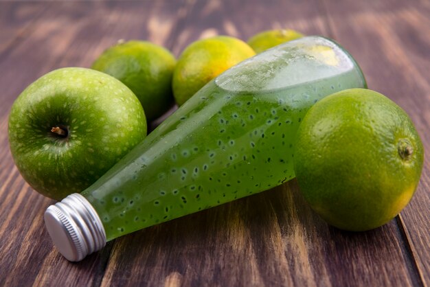 Botella de jugo de vista frontal con mandarinas verdes y manzana en la pared de madera