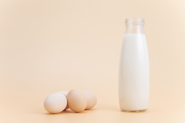 Botella de leche con algunos huevos sobre una superficie naranja