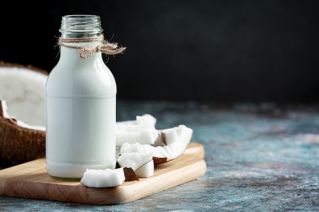 Botella de leche de coco puesta sobre tabla de cortar de madera