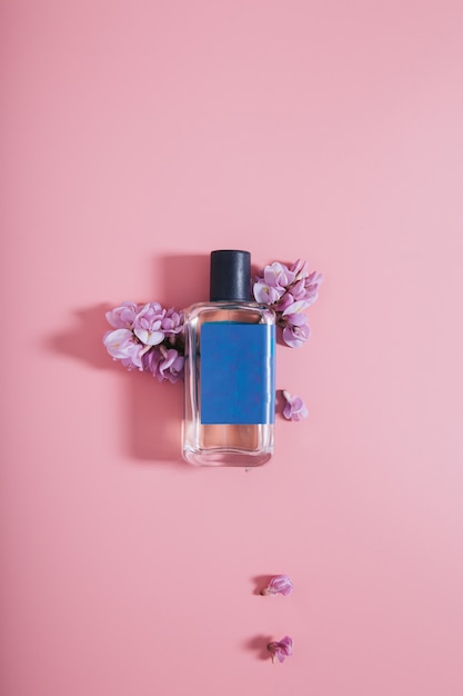 Botella de perfumes en pared rosa con flores