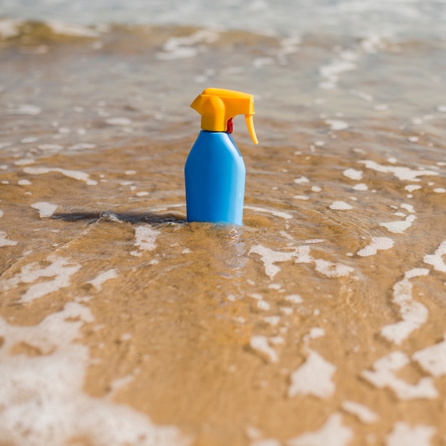 Botella de plástico protector solar azul en el agua de mar poco profunda en la playa