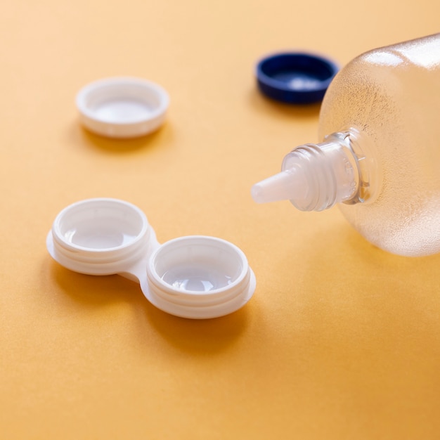 Botella con solución de lentes y caja de lentes sobre fondo naranja