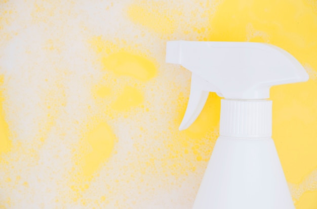 Foto gratuita botella de spray blanco contra jabón sobre fondo amarillo