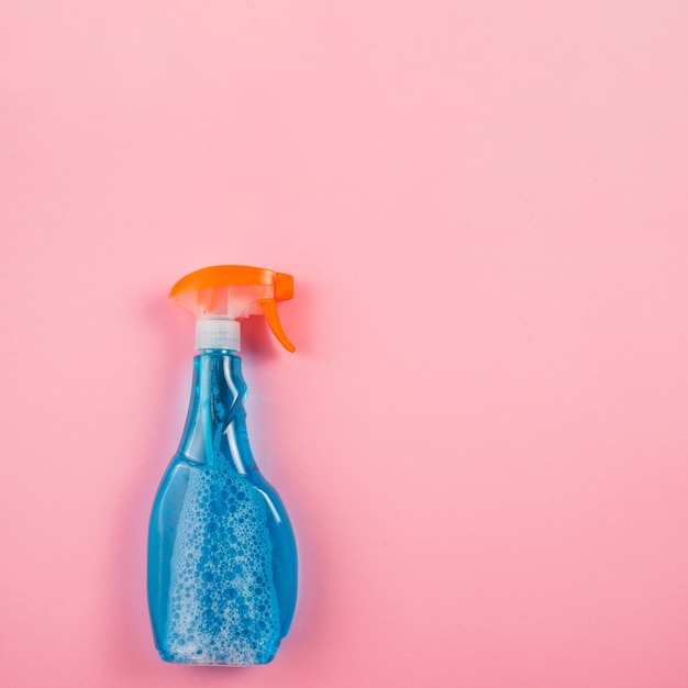 Foto gratuita botella de spray con líquido azul sobre fondo rosa