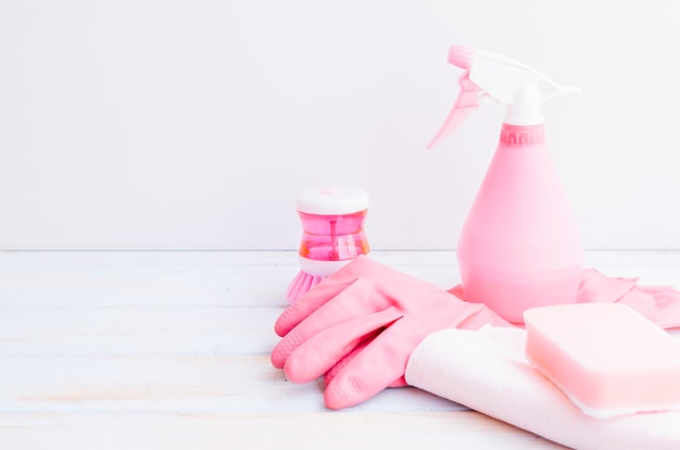 Botella de spray rosa; guantes; esponja en escritorio blanco contra la pared
