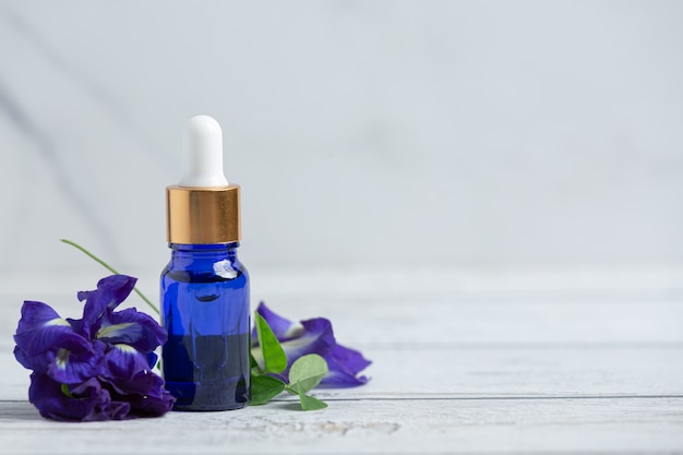 Botella de suero de aceite de flor de guisante de mariposa puesto sobre piso de madera blanca
