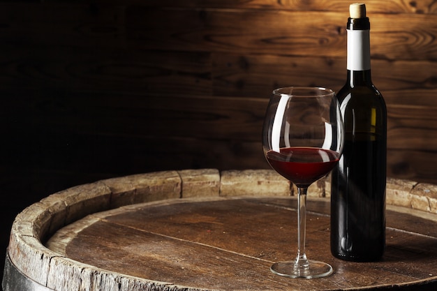 Botella y vaso de vino tinto en barril de madera con fondo de madera oscura