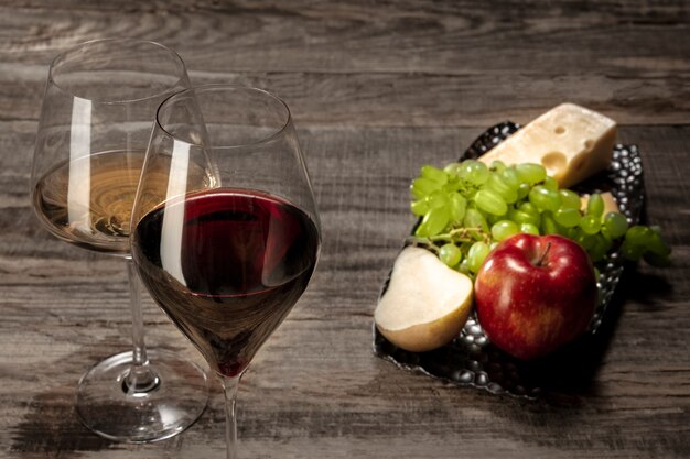 Una botella y vasos de vino tinto y blanco con frutas.