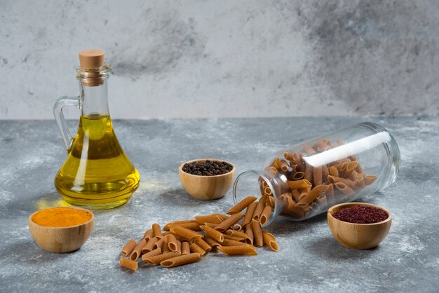 Una botella de vidrio de aceite con macarrones crudos.