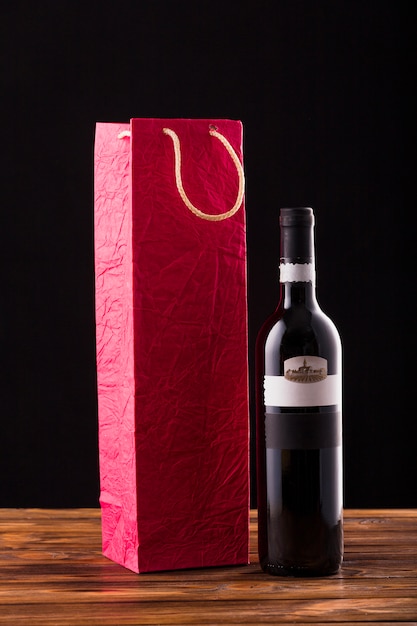 Botella de vino y bolsa de papel roja en mesa de madera con fondo negro