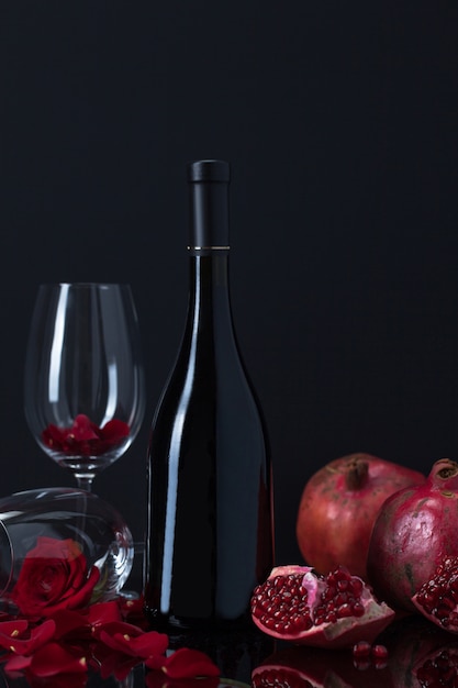 Foto gratuita botella de vino con copas, granadas y pétalos de rosa.