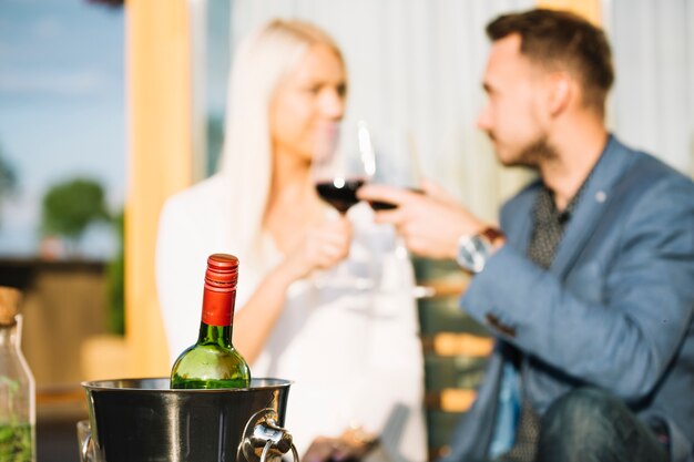 Botella de vino en el cubo de hielo con pareja tostado copas de vino