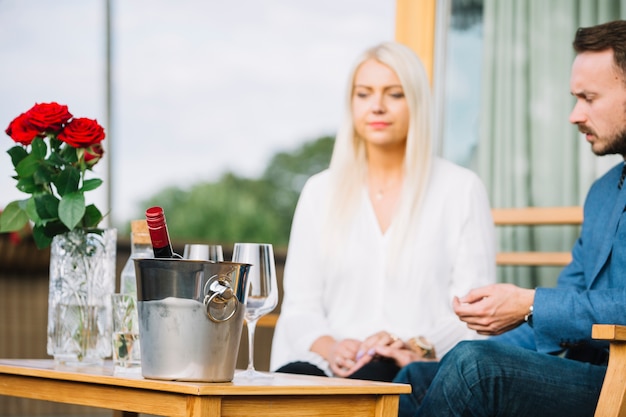 Botella de vino dentro del cubo de hielo en frente de la pareja sentados juntos