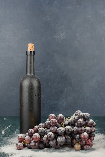 Botella de vino y racimo de uvas negras sobre mesa de mármol.