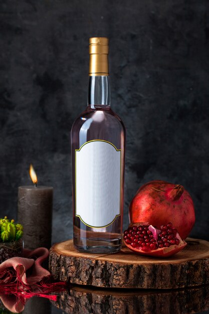 Botella de vino con vela, granada, planta y bufanda sobre una pieza de madera.