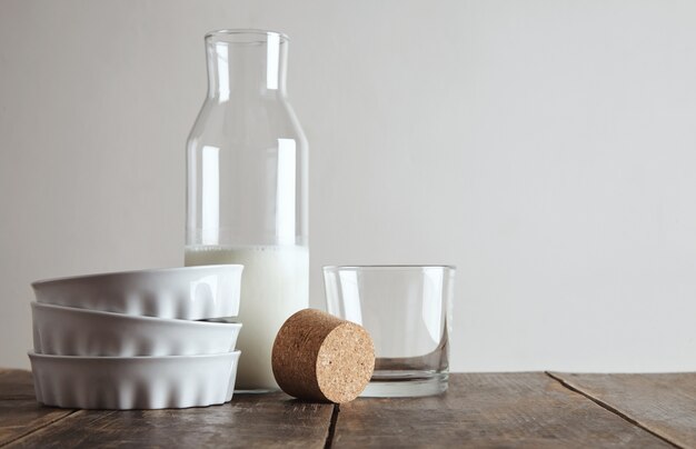 Botella vintage abrió corcho con leche en la mesa de madera envejecida cerca de whisky rox vidrio transparente y tres placas de cerámica, aislado en blanco