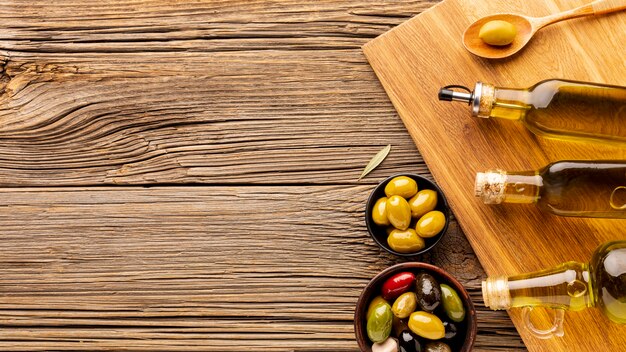 Botellas de aceite, cuencos de oliva y cuchara de madera con espacio de copia