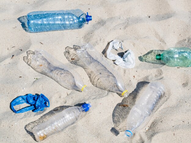 Botellas de agua plásticas vacías y bolsa de plástico sobre arena