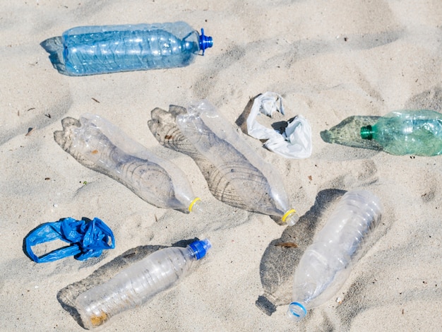 Botellas de agua plásticas vacías y bolsa de plástico sobre arena